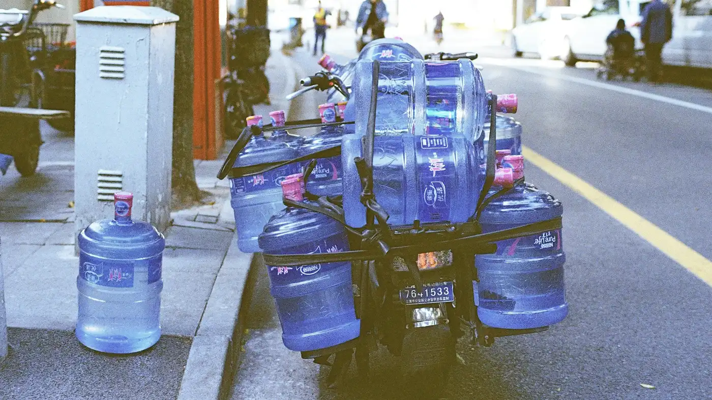 Moto de entrega carregada de galões de água de 20 litros, com um galão já deixado na calçada